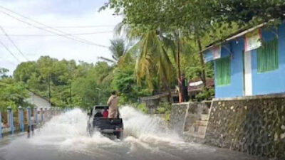 Sebuah mobil menerobos banjir yang merendam jalan utama.